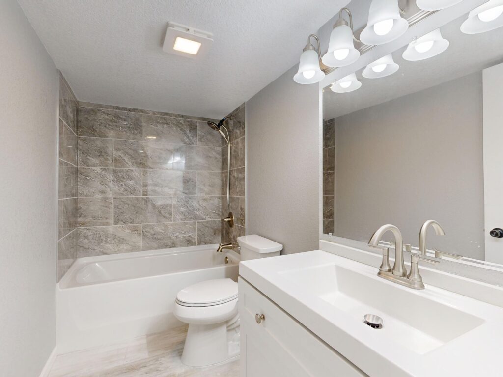 Finished bathroom remodel with a tiled tub and shower surround, quartz-topped vanity and chrome fixtures