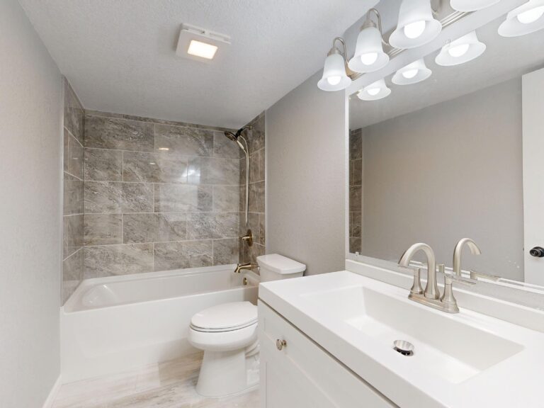 Finished bathroom remodel with a tiled tub and shower surround, quartz-topped vanity and chrome fixtures