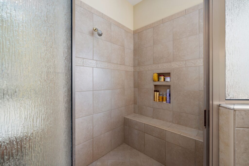 Tiled walk-in shower with a built-in recessed niche, bench seat and frameless glass panel