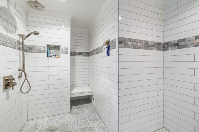 Open tiled shower area with floor-to-ceiling white wall tile, mosaic floor tile and a built-in seat