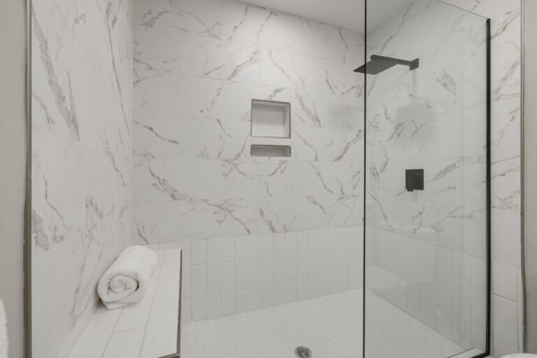 Walk-in shower with a fixed glass panel, marble-look wall tile, recessed niche and built-in bench